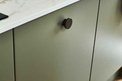 Close-up of Soho green Balmoral cabinet and black handles, with light gray marble worktop and white sink.