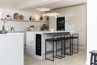 Diagnonal view of kitchen island corner in Yasmin Wyatt's open, light and airy neutral shade handleless Luna kitchen from Magnet with a white Corian worktop in Onyx, two AEG ovens integrated into tall cabinet and a wine cooler integrated into kitchen island.