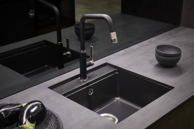 A contemporary kitchen with a matt black sink and tap, dark worktops and modern black glass splashback.