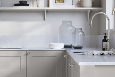 Ludlow, a traditional Shaker-style premium feel kitchen range with a visible woodgrain on its panelled doors here shown in the light grey shade Dove grey styled with steel knobs, steel tap, a white marbled worktop with matching splashback.