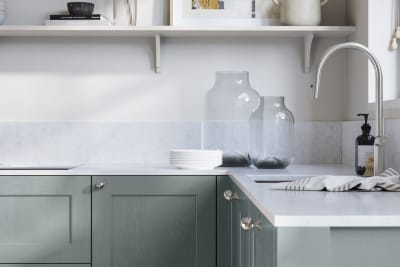 Ludlow, a traditional Shaker-style premium feel kitchen range with a visible woodgrain on its panelled doors here shown in the light blue shade Duck Egg styled with steel knobs, steel tap, a white marbled worktop with matching splashback.