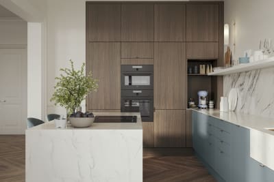 Soho Duck Blue kitchen from Magnet combined with ovens integrated into tall Nordic Nature cabinetry, white marble splashblack, paired beautifully with a bright brass tap and sink.