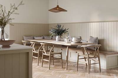 Traditional Shaker-style Ludlow Parchment bench cabinets with tactile woodgrain, a kitchen island and matching wall panel, a long wood diningroom table with matching wood chairs and ceramics set out on the table.