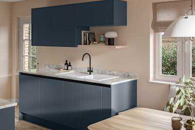 Handleless Integra Ascoli Mineral Blue, a dark blue kitchen with a wood wall shelf, rounded matt black tap with white sink, a white and grey marbled worktop with matching upstand.