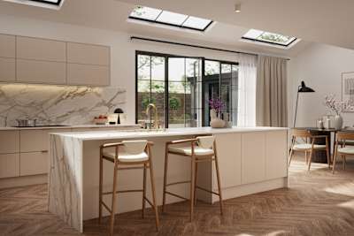 Fluted front kitchen Reed from Magnet in light warm neutral shade Shell, with a marbled splashback, worktop and decorative side on kitchen island with barstools and black handles, herringbone wood flooring.