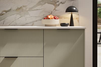 Fluted front kitchen Reed from Magnet in neutral shade French Clay, with a marbled splashback and black handles, herringbone wood flooring.