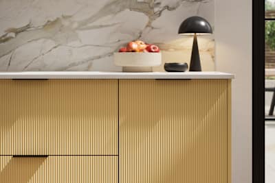 Fluted front kitchen Reed from Magnet in bright yellow shade Harvest, with a marbled splashback and black handles, herringbone wood flooring.