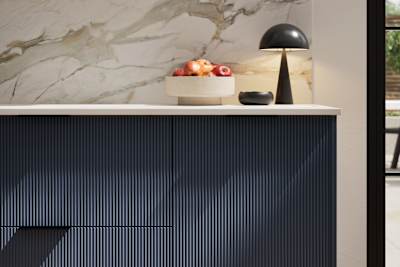 Fluted front kitchen Reed from Magnet in dark blue shade Midnight, with a marbled splashback and black handles, herringbone wood flooring.