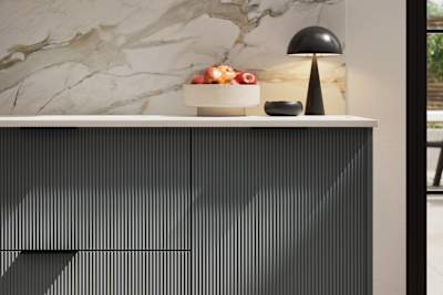 Fluted front kitchen Reed from Magnet in dark green shade Arboretum, with a marbled splashback and black handles, herringbone wood flooring.