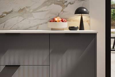 Fluted front kitchen Reed from Magnet in dark grey shade Charcoals, with a marbled splashback and black handles, herringbone wood flooring.