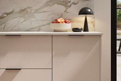 Fluted front kitchen Reed from Magnet in light neutral shade Shell, with a marbled splashback and black handles, herringbone wood flooring.