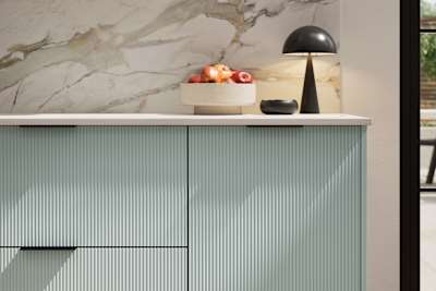 Fluted front kitchen Reed from Magnet in bright blue shade Sky, with a marbled splashback and black handles, herringbone wood flooring.