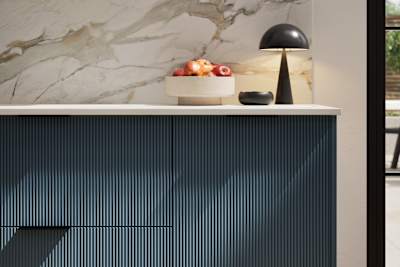 Fluted front kitchen Reed from Magnet in dark blue shade Voyage Blue, with a marbled splashback and black handles, herringbone wood flooring.