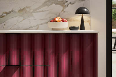 Fluted front kitchen Reed from Magnet in red shade Morello, with a marbled splashback and black handles, herringbone wood flooring.