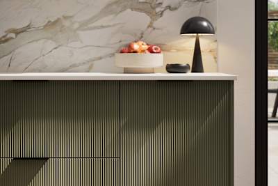 Fluted front kitchen Reed from Magnet in dark green shade Tailored Green, with a marbled splashback and black handles, herringbone wood flooring.