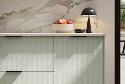 Fluted front kitchen Reed from Magnet in light green shade Seagrass, with a marbled splashback and black handles, herringbone wood flooring.