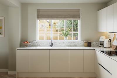 Open plan light neutral shade fluted kitchen with integrated appliances, white and grey marble worktop and upstand. Herringbone wood flooring.