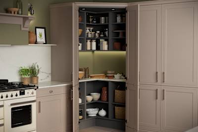 Opened walk-in pantry in Shaker style painted wood grain Bewdley kitchen in neutral shade Cornish Clay, tall cabinets with marbled worktop and matching backsplash and gas range cooker.