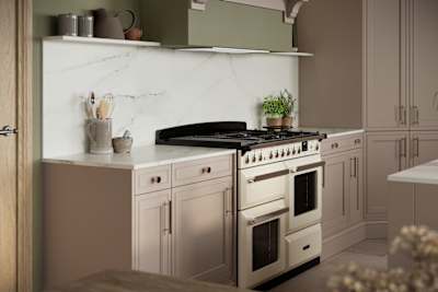 Gas range cooker in Shaker style painted wood grain Bewdley kitchen in neutral shade Cornish Clay, tall cabinets with marbled worktop and matching backsplash, traditional knobs and handles.
