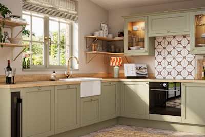 Close-up view of contemporary Shaker kitchen Ambleside from Magnet in sage green shade Meadow with belfast sink, aged taps and wooden effect worktop.