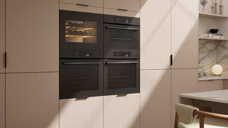Fluted front kitchen Reed from Magnet in light warm neutral shade Shell, tall cabinets with appliances like ovens and a wine cooler, black handles