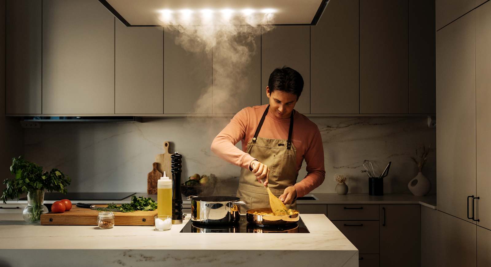 Filip Poon lagar mat i sitt clean och eleganta Arkitekt Plus Sand-kök från Marbodal med Dekton-bänkskiva och matchande stänkskydd