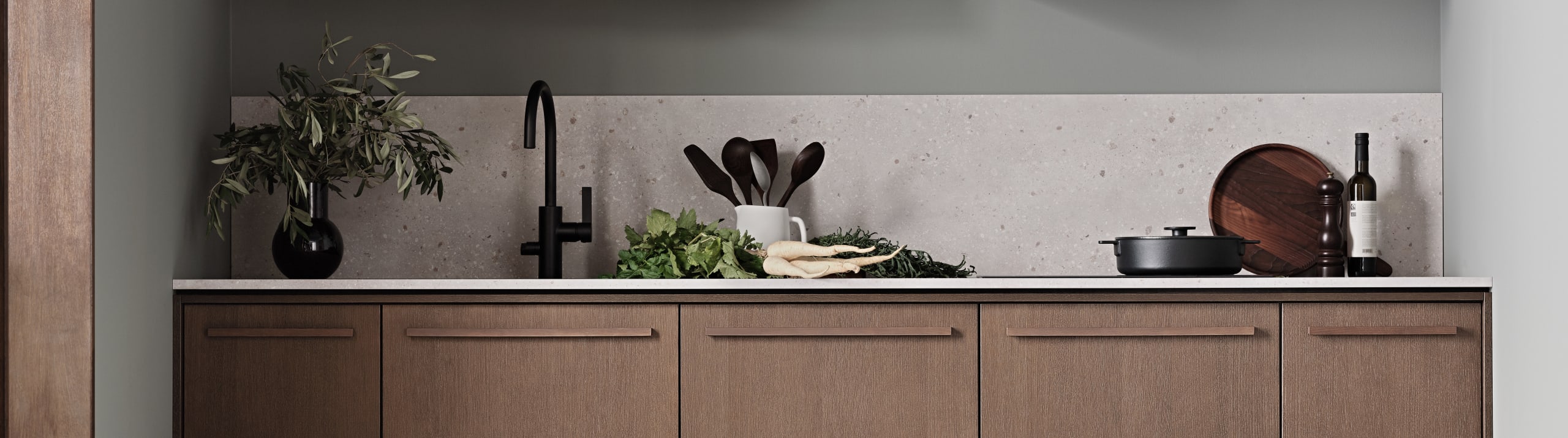 Køkken Forever Oak fra INVITA, mørk eg køkkenskabe med massiv tre mørk eg håndtag, komposit bordplade, sort armatur og vitrineskab med riflede glas i tynd, sort aluminiumsramme