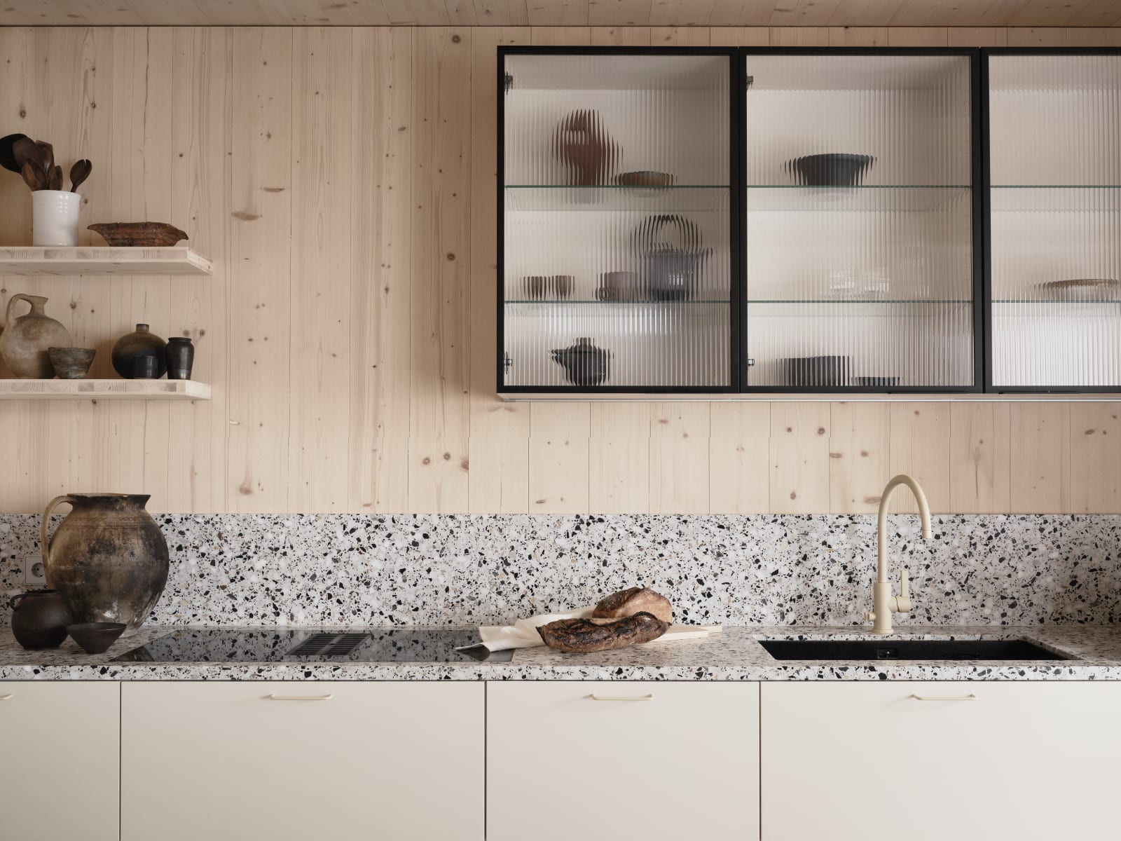 Beige blandare och svart diskho i terrazzo-bänkskiva med matchande stänkskydd, vitrinskåp med räfflat glas i Edd Ruchtons Grand design kök i beige Arkitekt Plus-kök från Marbodal