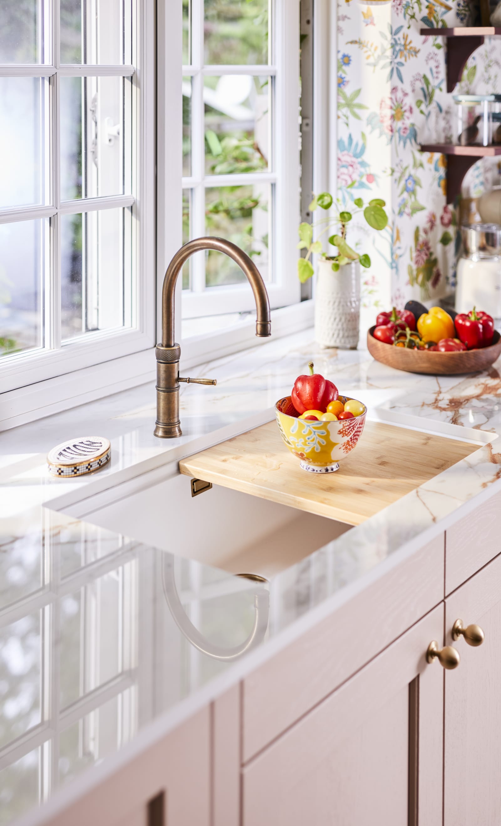 View of quooker brass tap, white sink and fresh vegetables in bowl on a cutting board.