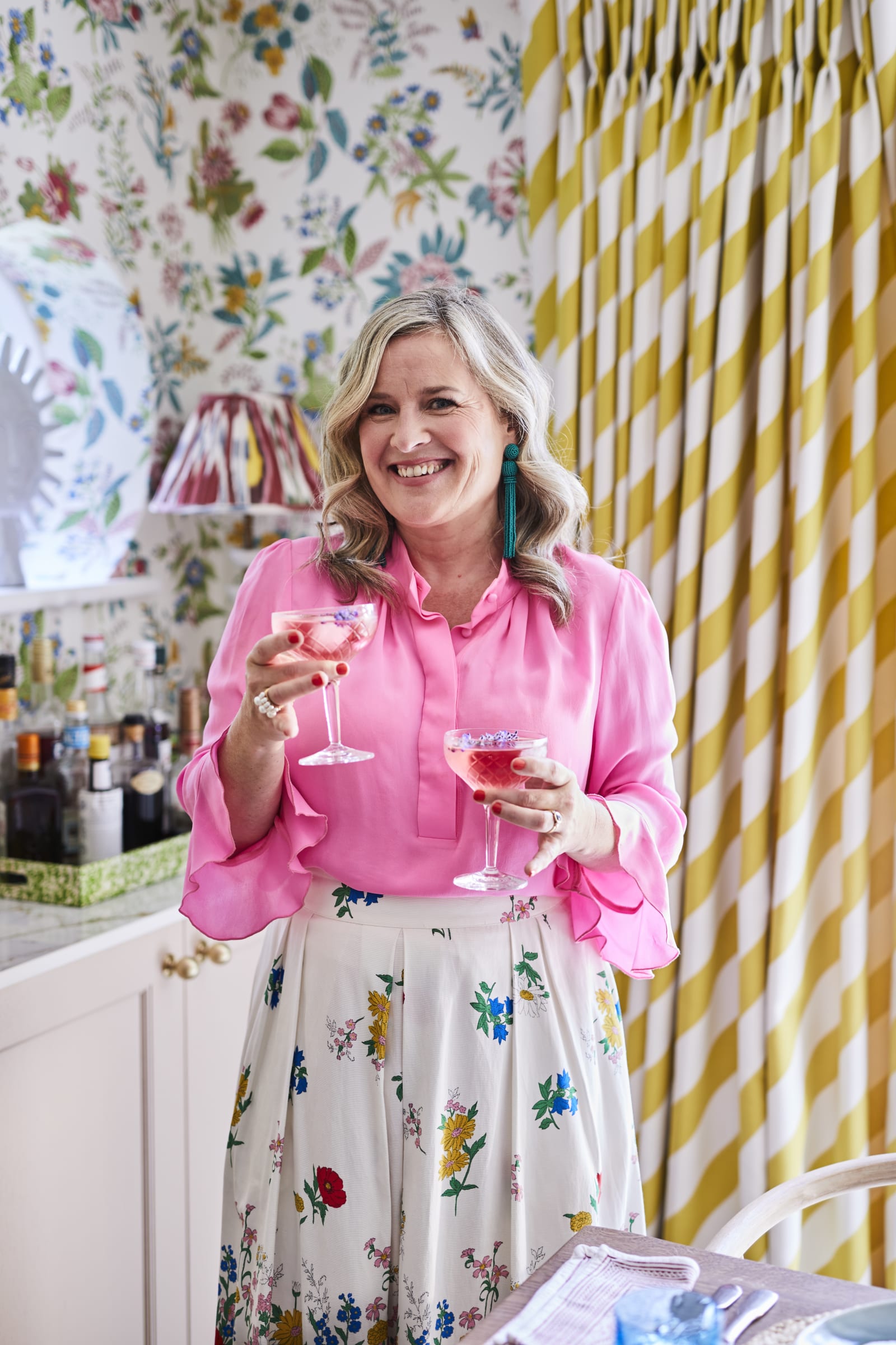 Sophie smiling and wearing vibrant colors, holding two drinks in the Cocktail corner