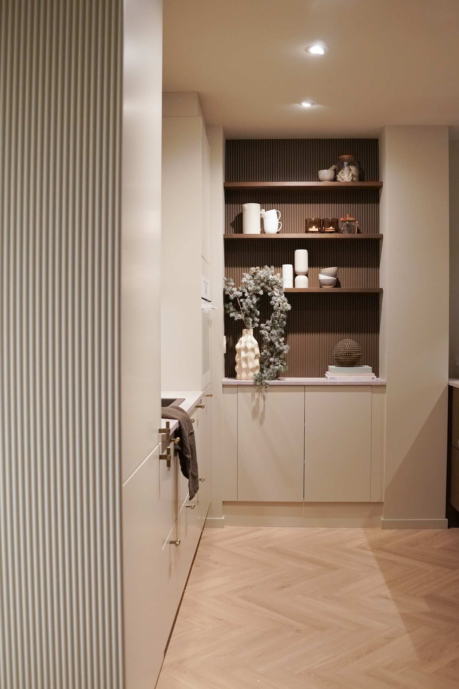 Veggen i kaffenisjen, der hyllene er festet er dekket med rillede dekorplater fra Deco Systems, malt i en egenkomponert farge som ligner beisfargen på kjøkkenøya