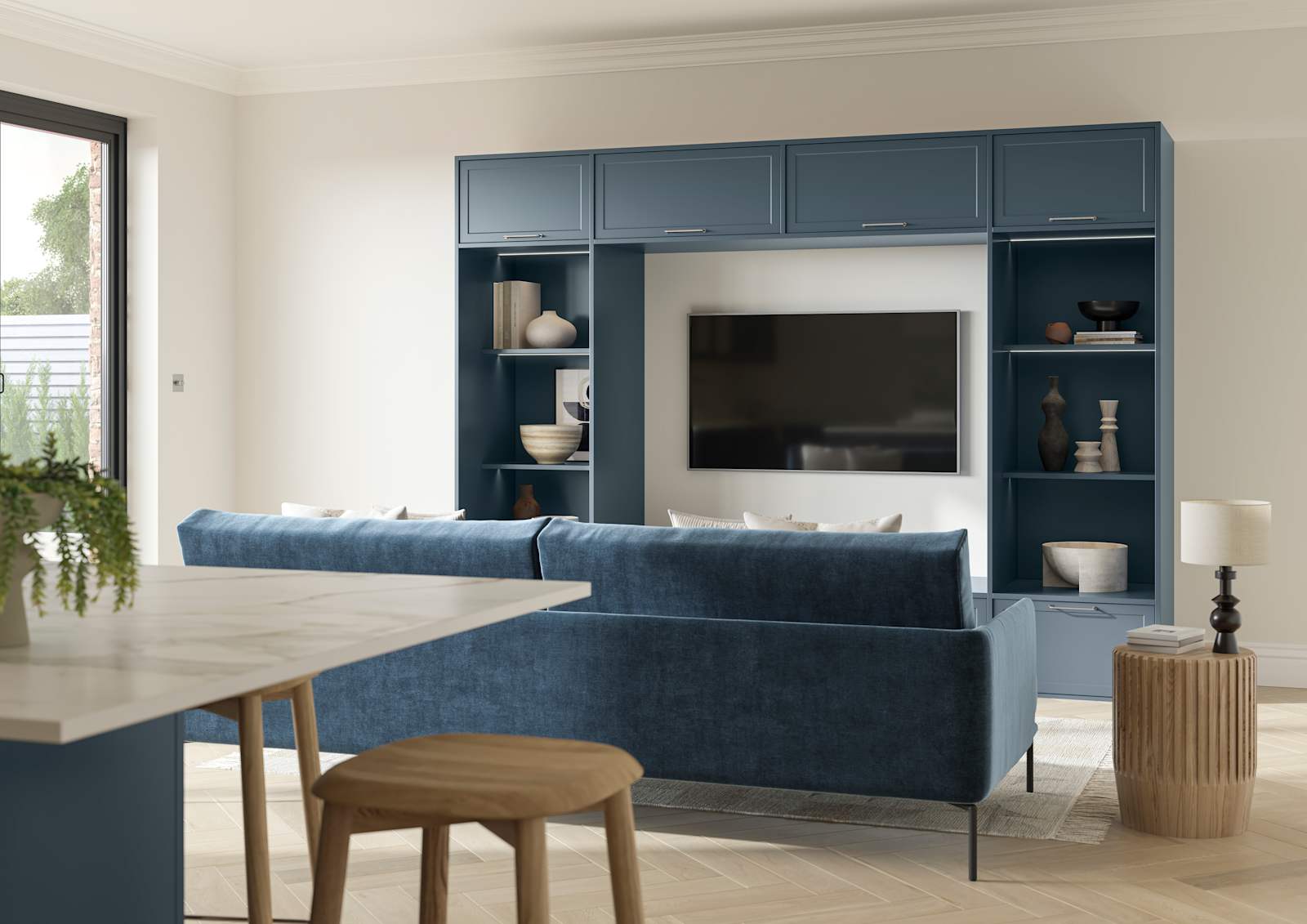 Cabinets and open shelves around a wall mounted TV in the modern Shaker range Brunswick Voyage Blue, matching blue counch and kitchen island in the foreground.