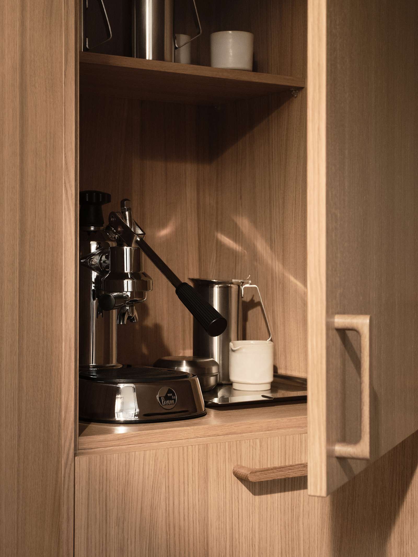 Öppnat skåp i Siri Barjes kök, ekskåp med kaffemaskin i skåpet, handtag i ek.