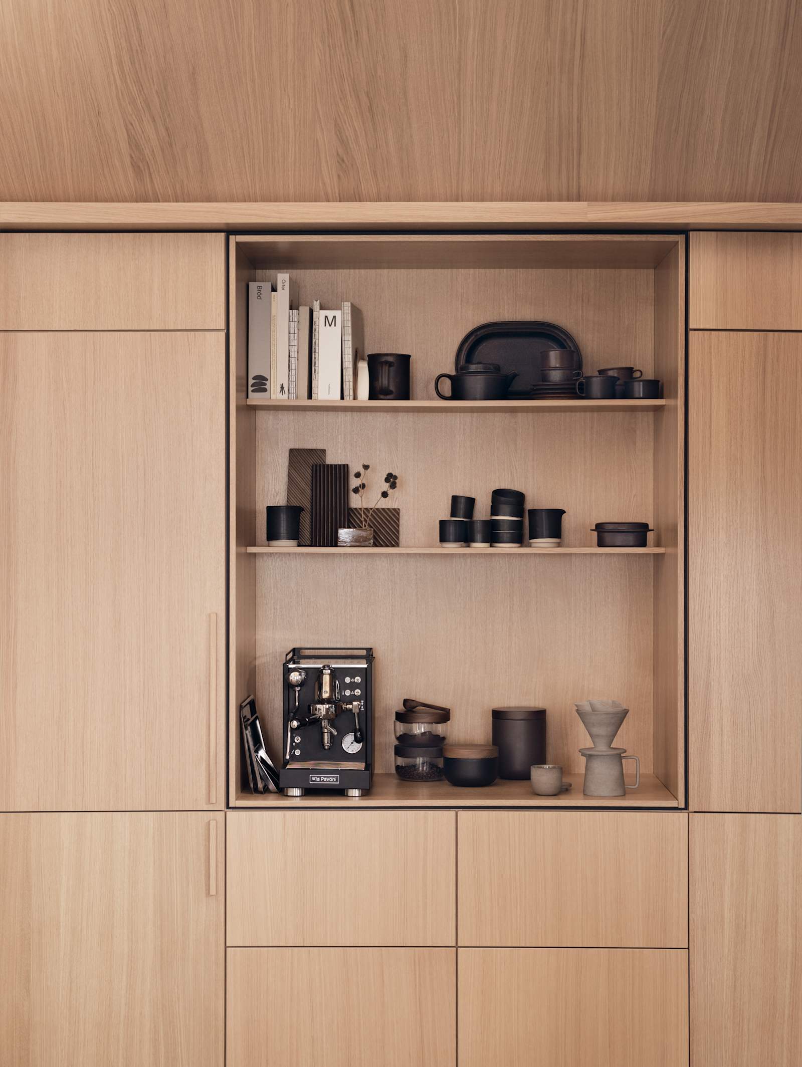 Køkkenet Forever Oak Natur Eg fra INVITA i egetræsfiner med lodret træåring, høje skabe og et åbent skab med plads til en kaffemaskine, indrammet med en skygge, der skaber et arkitektonisk premium-præg.