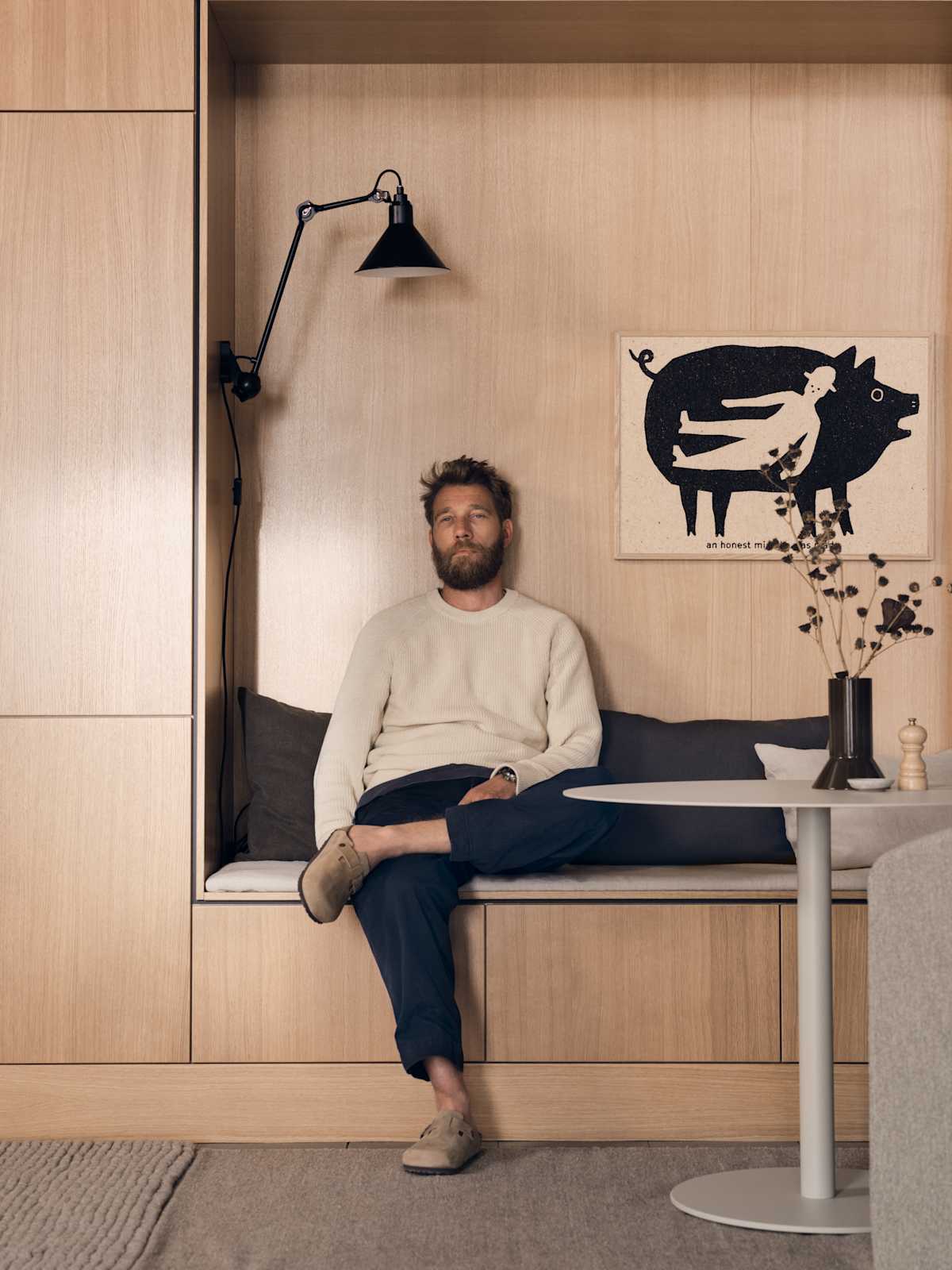 En mann sitter på en benk i nisjen på eikekjøkkenet Favn Natur fra Sigdal i eikefiner med vertikal trestruktur. Høyskap ved siden av nisjen som er innrammet med en skyggelegging, noe som skaper en arkitektonisk premiumfølelse.