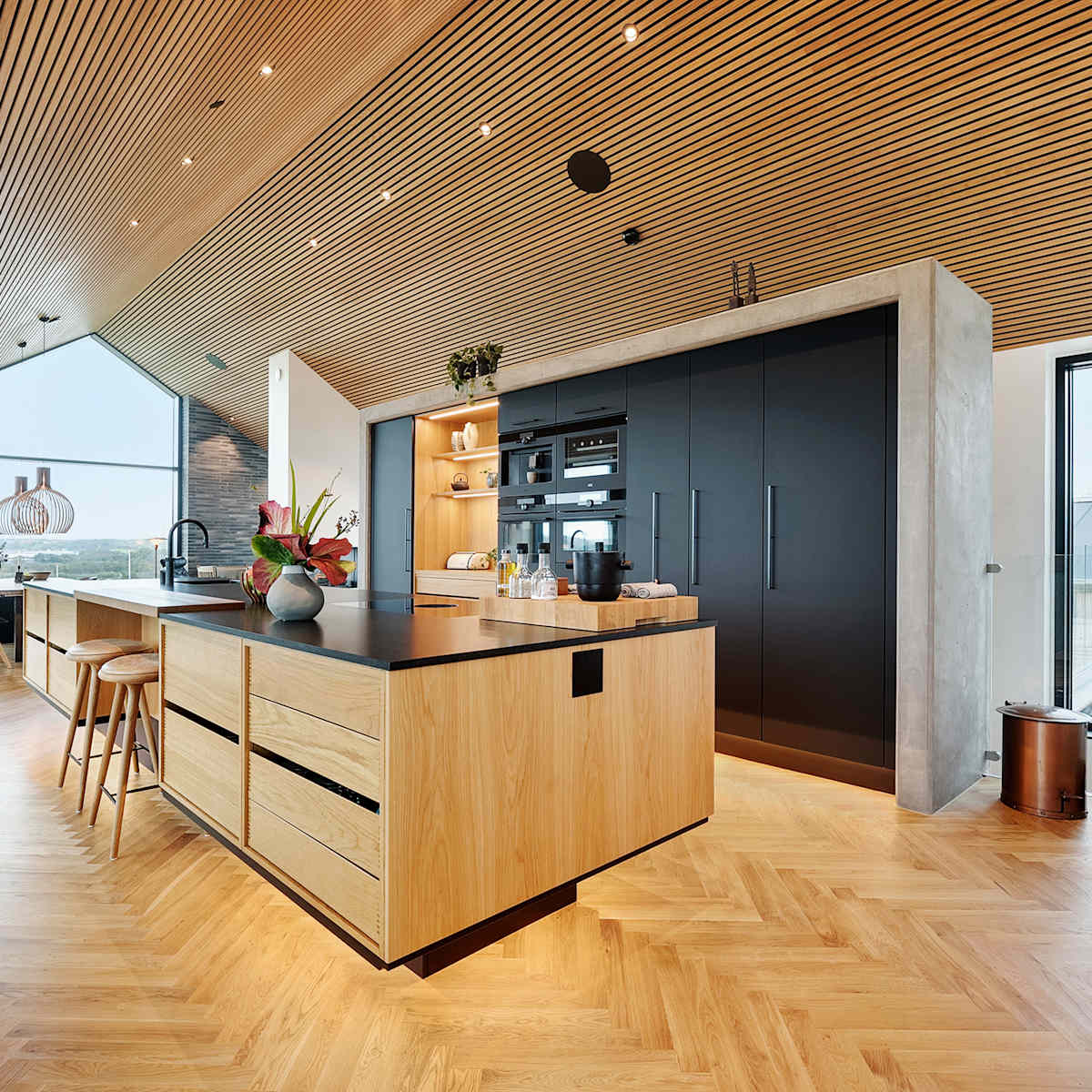 Köksö i ek och högskåp i mattsvart laminat i arkitektritat hus med utsikt över Limfjorden