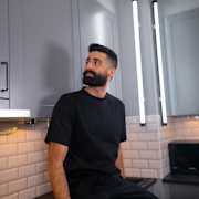 Simon Kafi sitter på köksbänken i sitt kök från Marbodal, mörkgrå ramlucka Form Åska med svarta handtag och svart bänkskiva med stänkskydd i vitt kakel