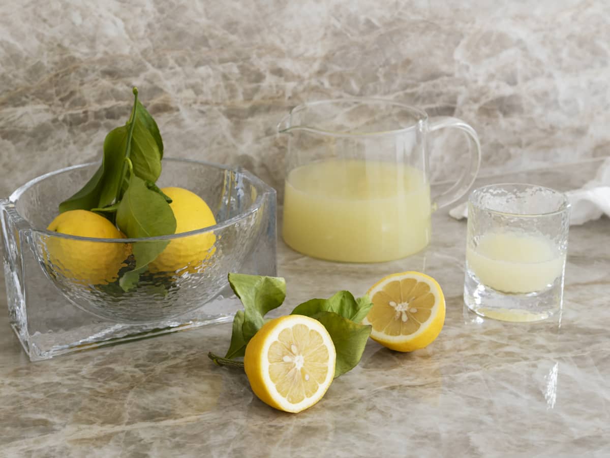 En glasskål med citroner, en kande og et drikkeglas med citronsaft
