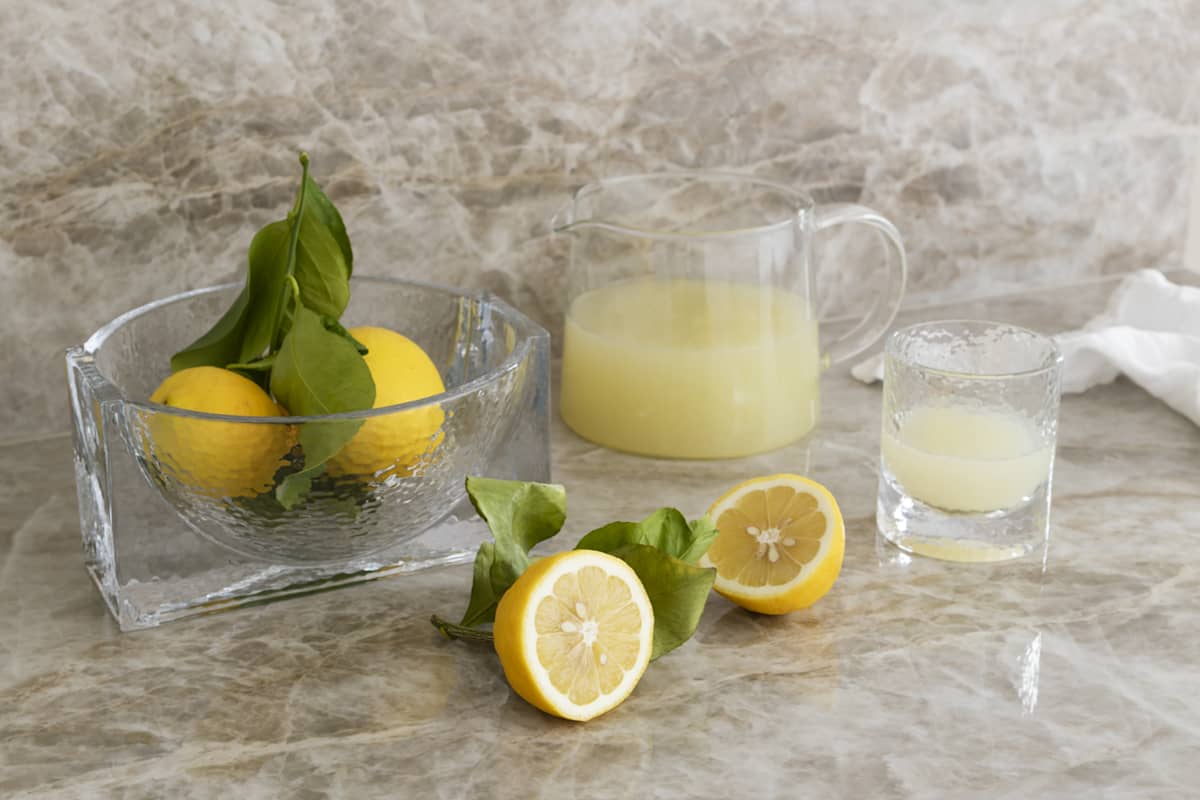 En glassbolle med sitroner, en kanne og et drikkeglass med sitronsaft