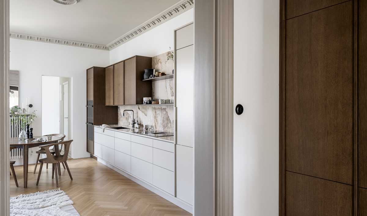 Kjøkken med kombinasjon av kjøkkenbenk i beige Line Korn med overskap i Signature Favn, finert eikedør i brunbeiset Nøtt fra Sigdal, matchende benkeplate og sprutbak, og åpne vegghyller i brunbeiset eikefiner.