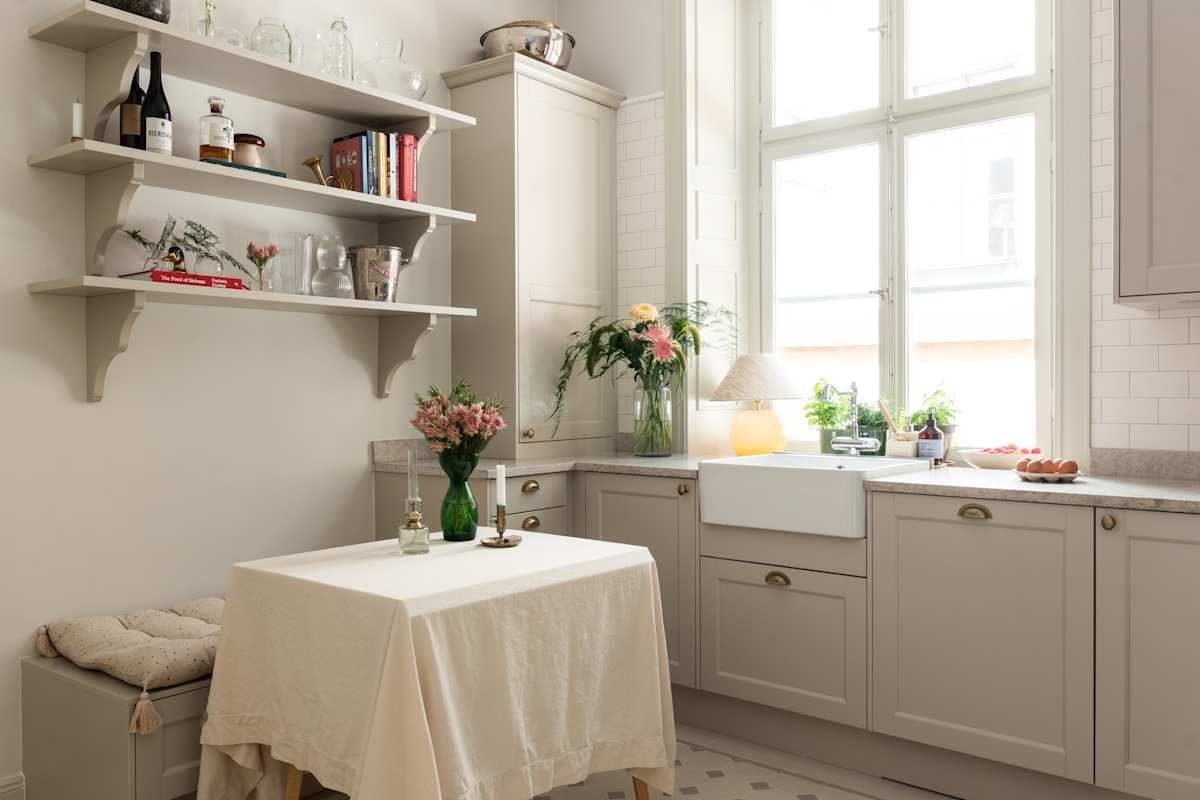 Sandra Beijers kök från Marbodal, Fagerö i den beige kulören Sand, med matchande öppna vägghyllor, en sittbänk med förvaring, diskho i porslin och handtag i mässing.