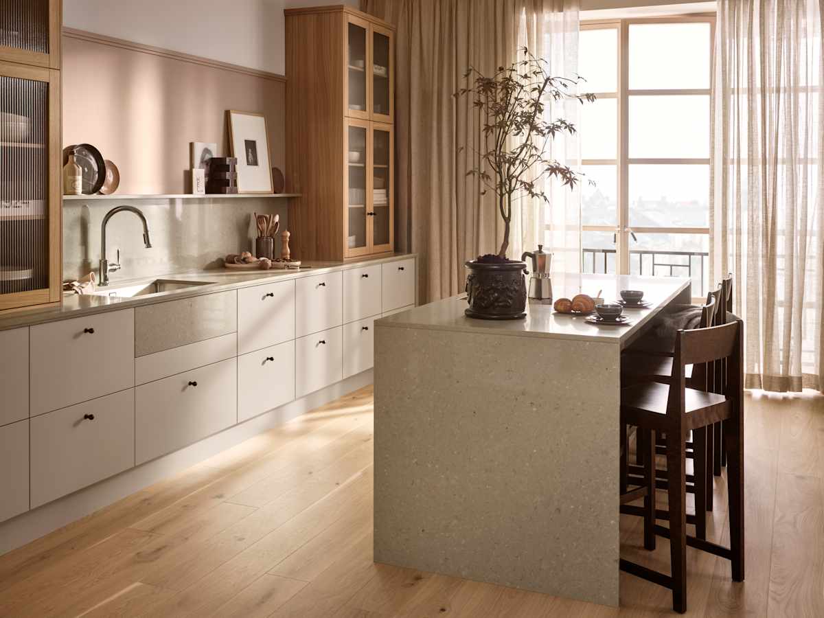 Köksö i beige köket Arkitekt plus gryning från Marbodal, med bardisk i köksön, belfast diskho, vitrinskåp med träram i ek och räfflat glas ovanpå köksbänken