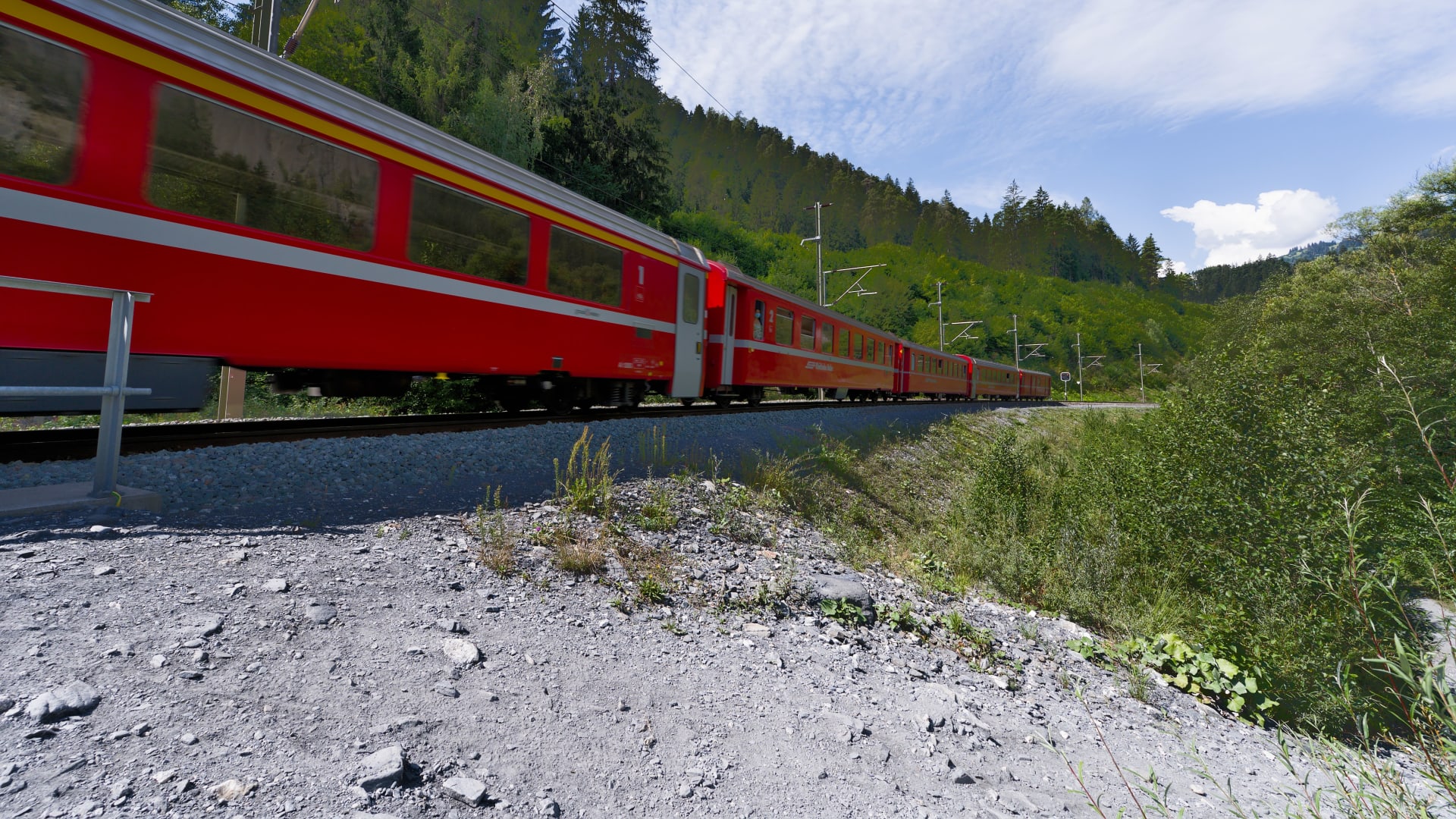 A red train curving through green hills