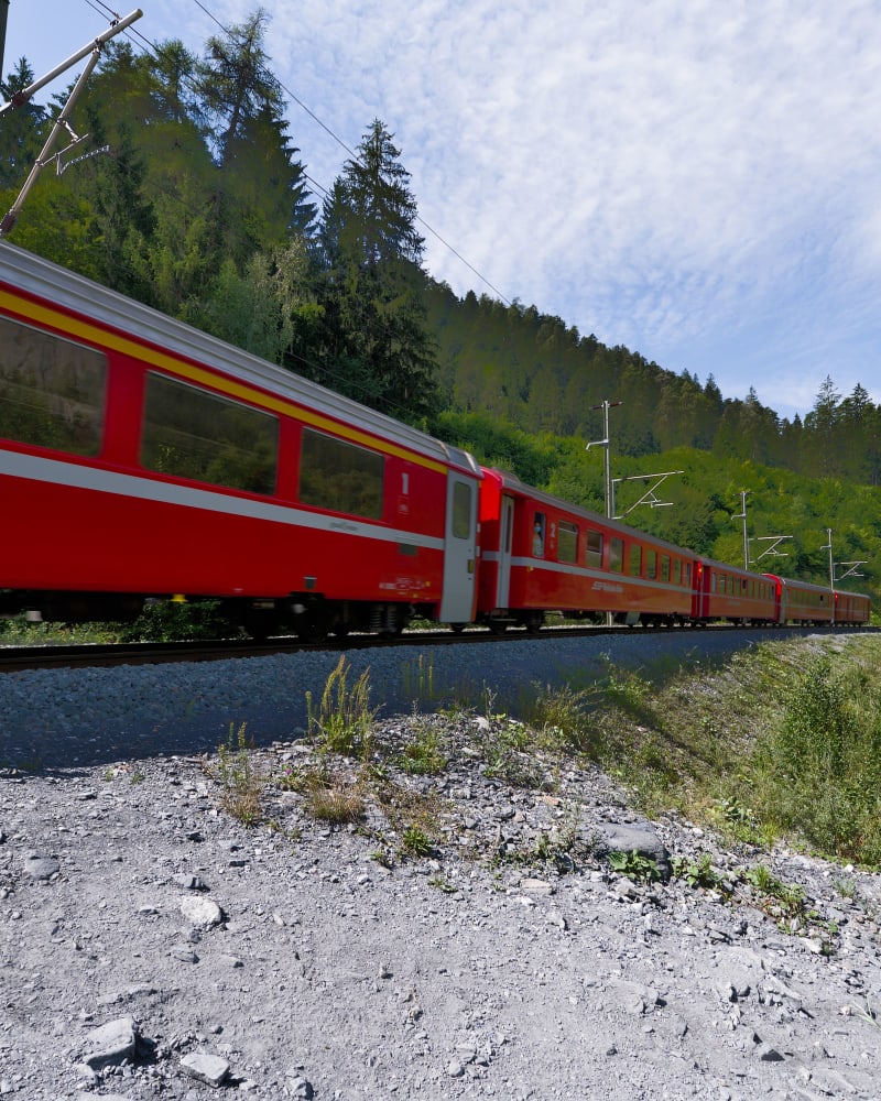 A red train curving through green hills
