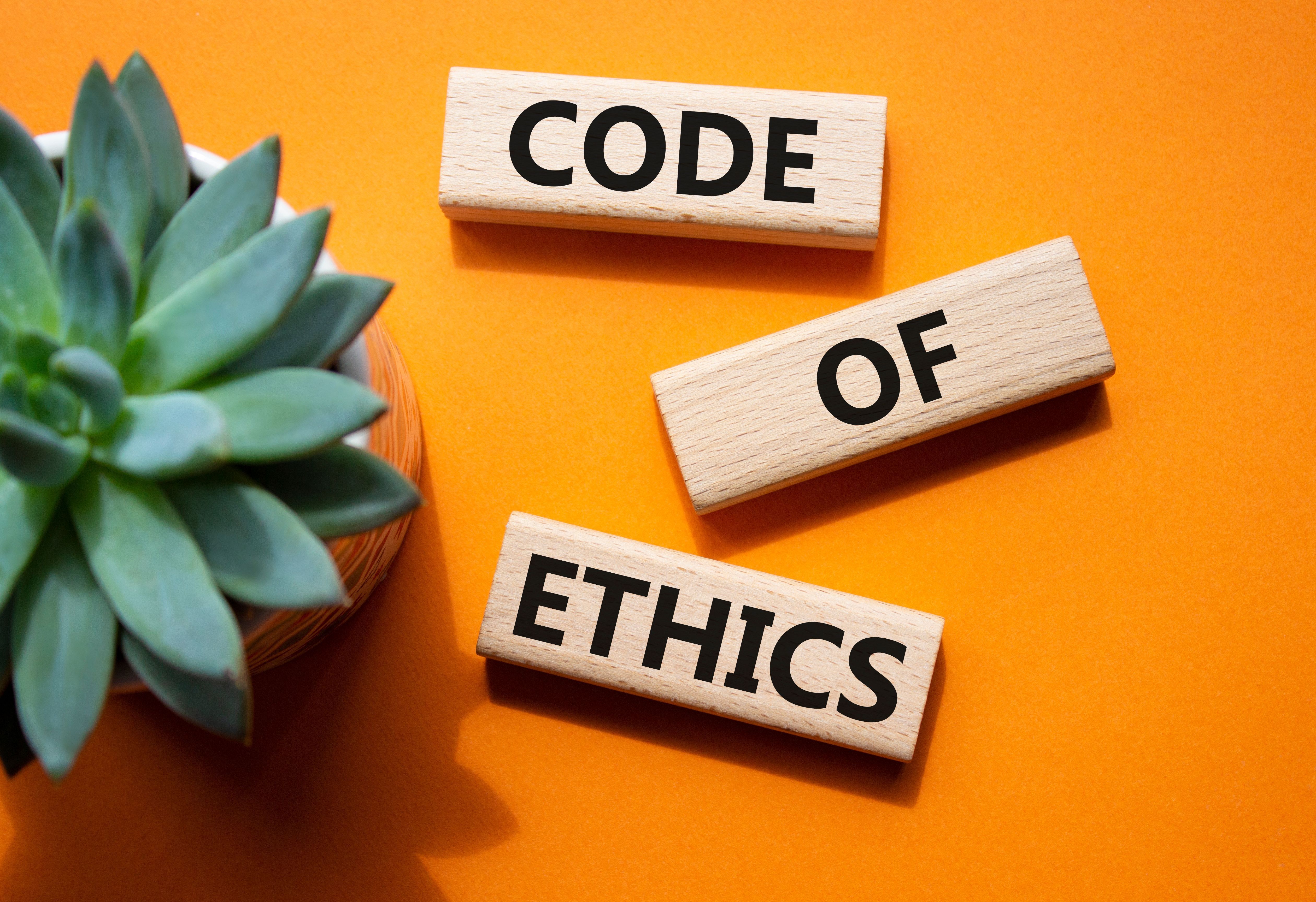 Wooden blocks spelling code of ethics on an orange background