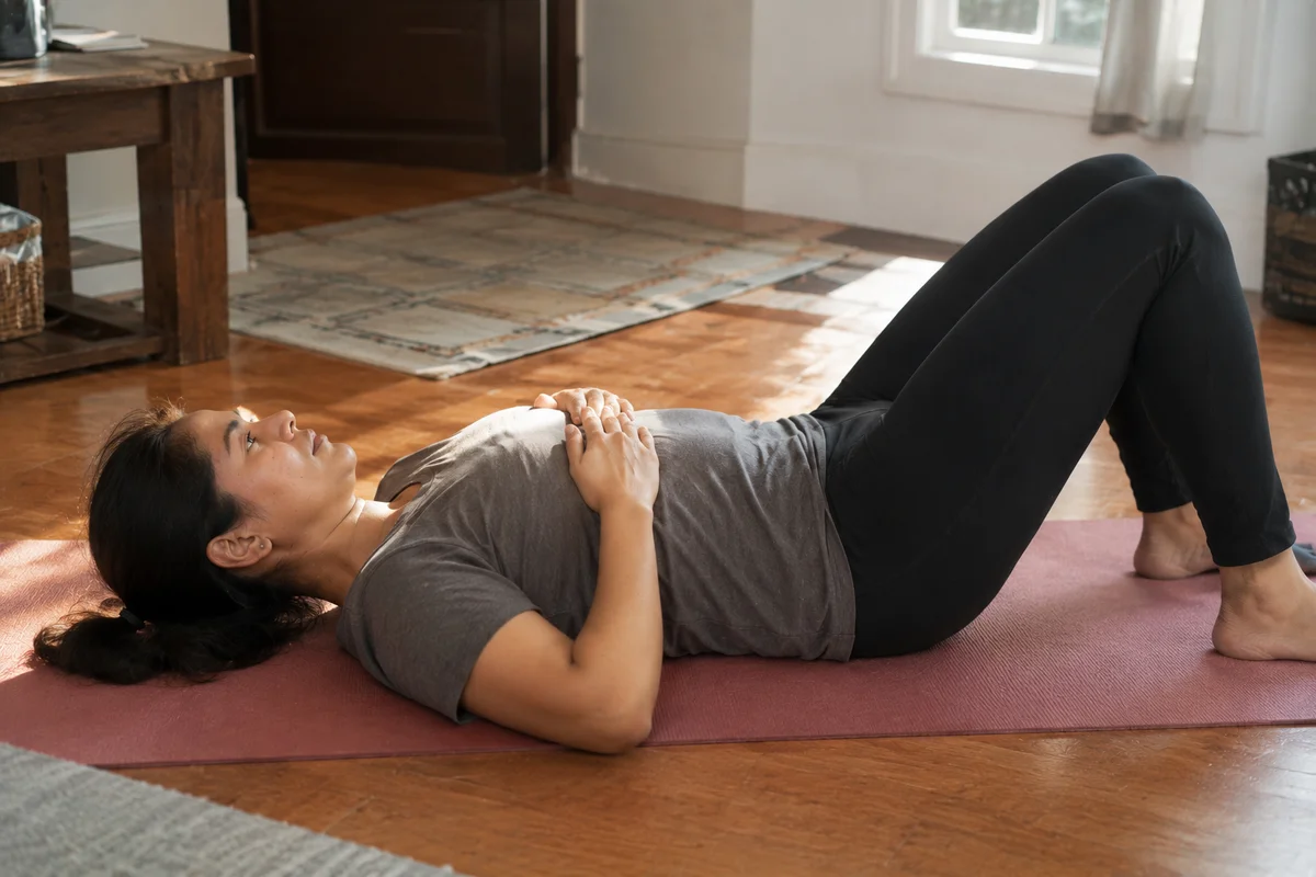 A mother lying on a yoga mat practicing pelvic tilts and breathing exercises, focusing on safe rehabilitation of her core after pregnancy.