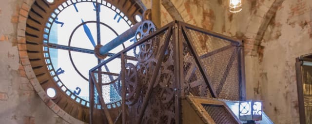 steampipe cage with gears beside a giant clock face and screen console, stone interior — Escape the Room Philadelphia, from its own website