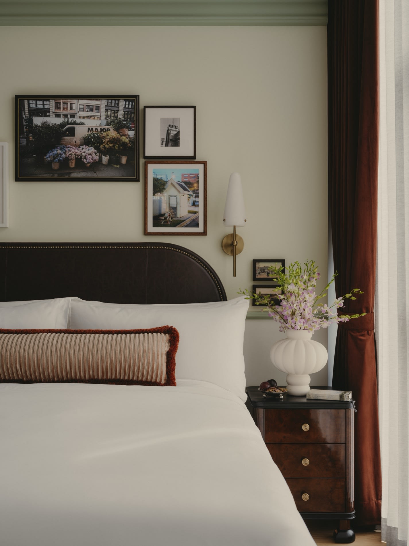Bett in einem Zimmer des NoMad Singapore mit Lederkopfteil und gerahmten Gemaelden