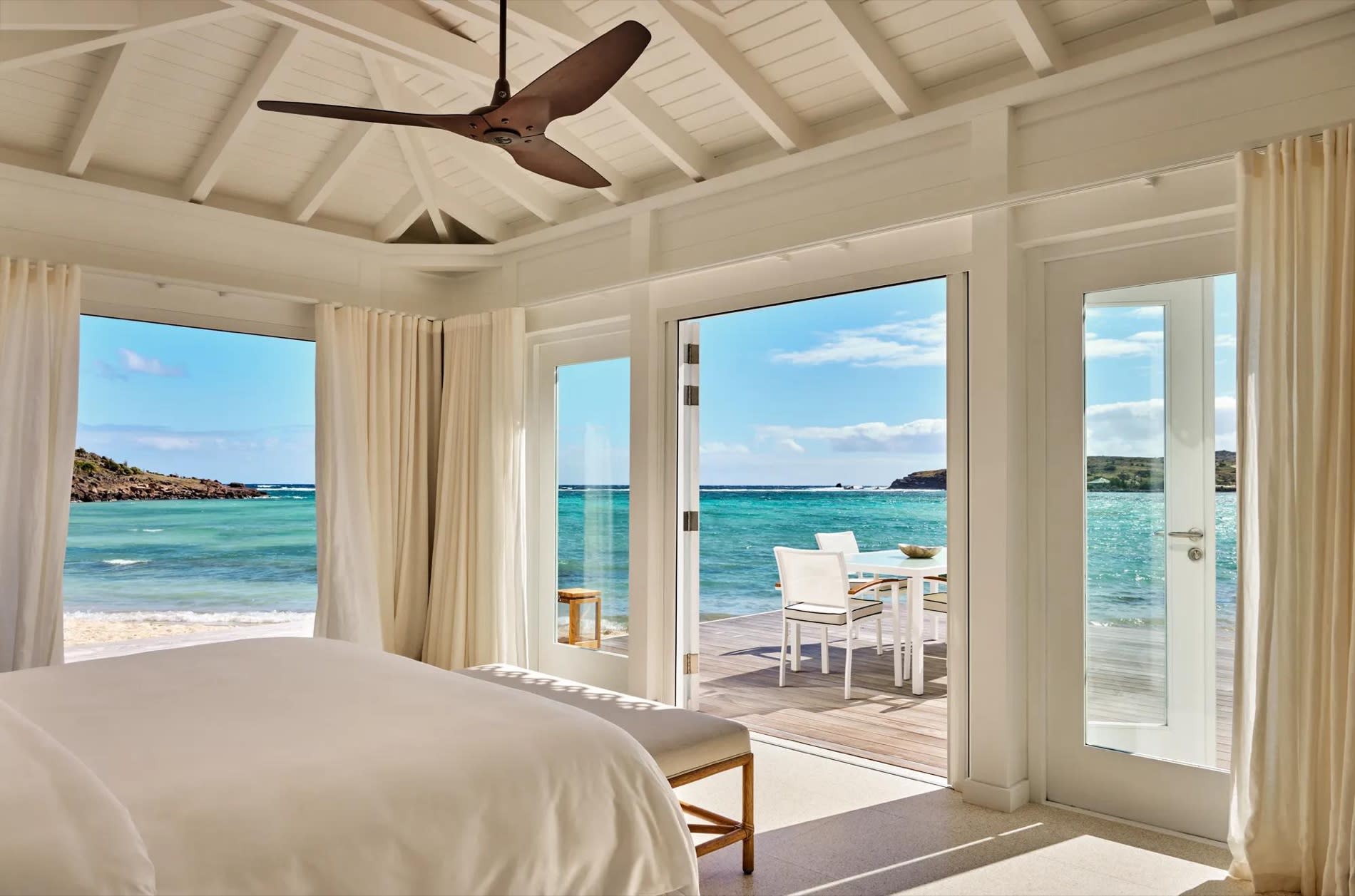 Bedroom of a Lagoon Suite at the Guanahani, white bed opening onto a terrace and the lagoon