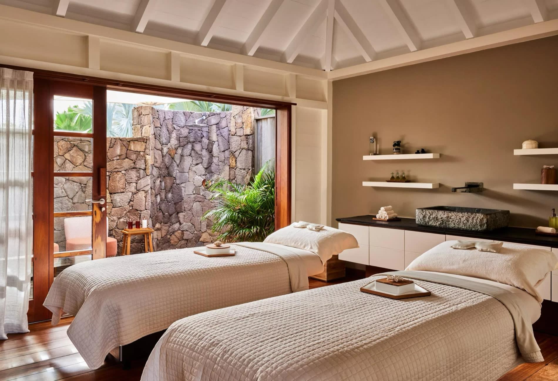 Duo treatment room at the Guanahani spa, two massage tables and stone wall opening onto the garden